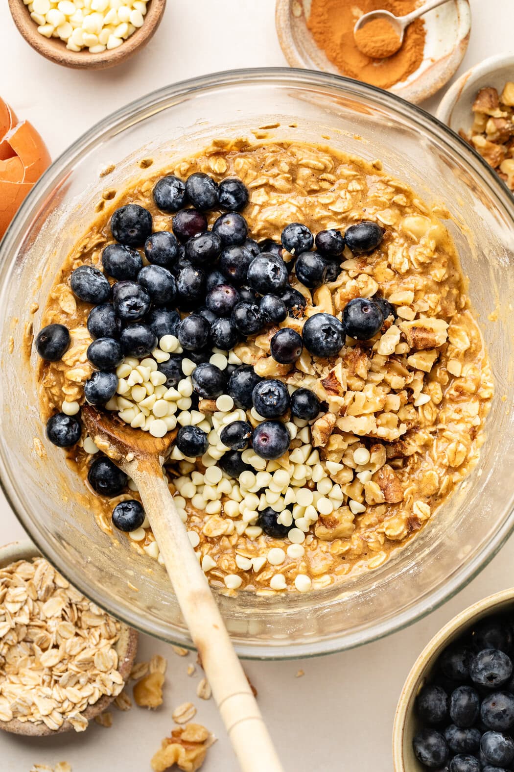 Overhead view of a glass bowl of Blueberry Oatmeal Breakfast Cookie batter topped with bright blueberries and white chocolate chips.