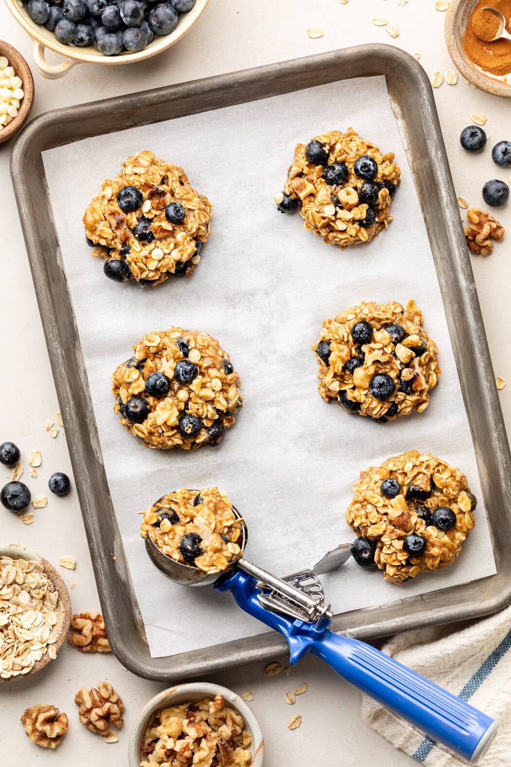 Overhead view of a sheet pan lined with white parchment paper and topped with six Blueberry Oatmeal Breakfast Cookies. 