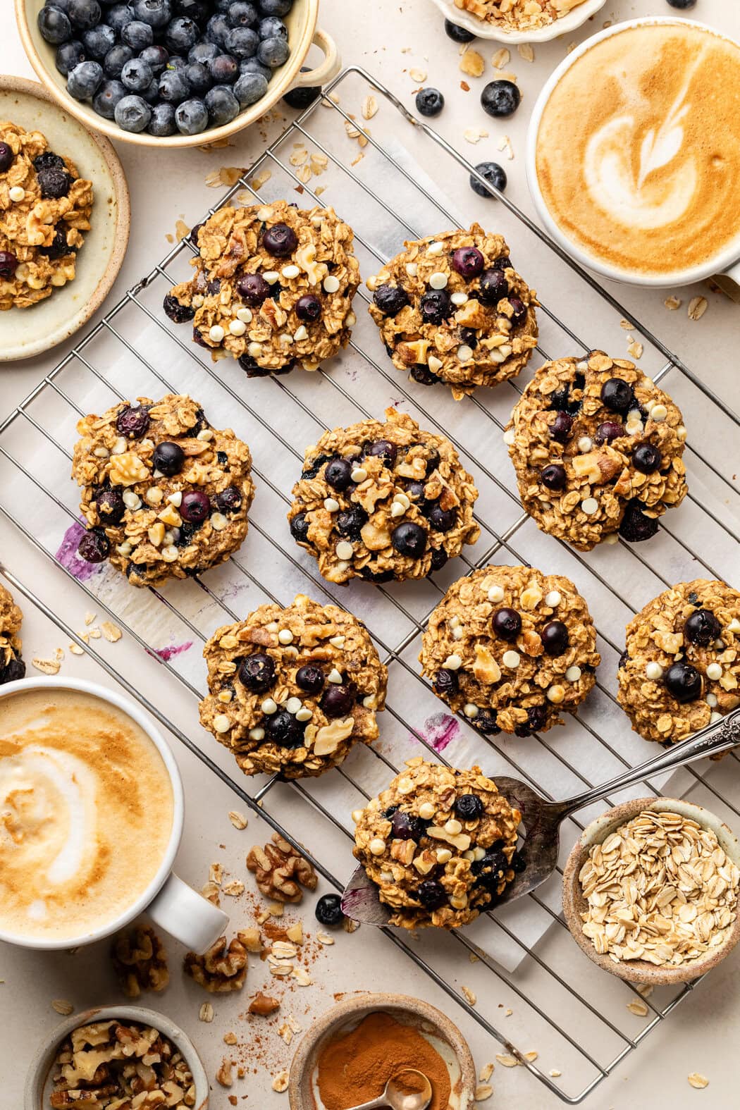 Close up view of Blueberry Oatmeal Breakfast Cookies on a cooling rack topped with white mini chocolate chips and a frothy latte on the side. 