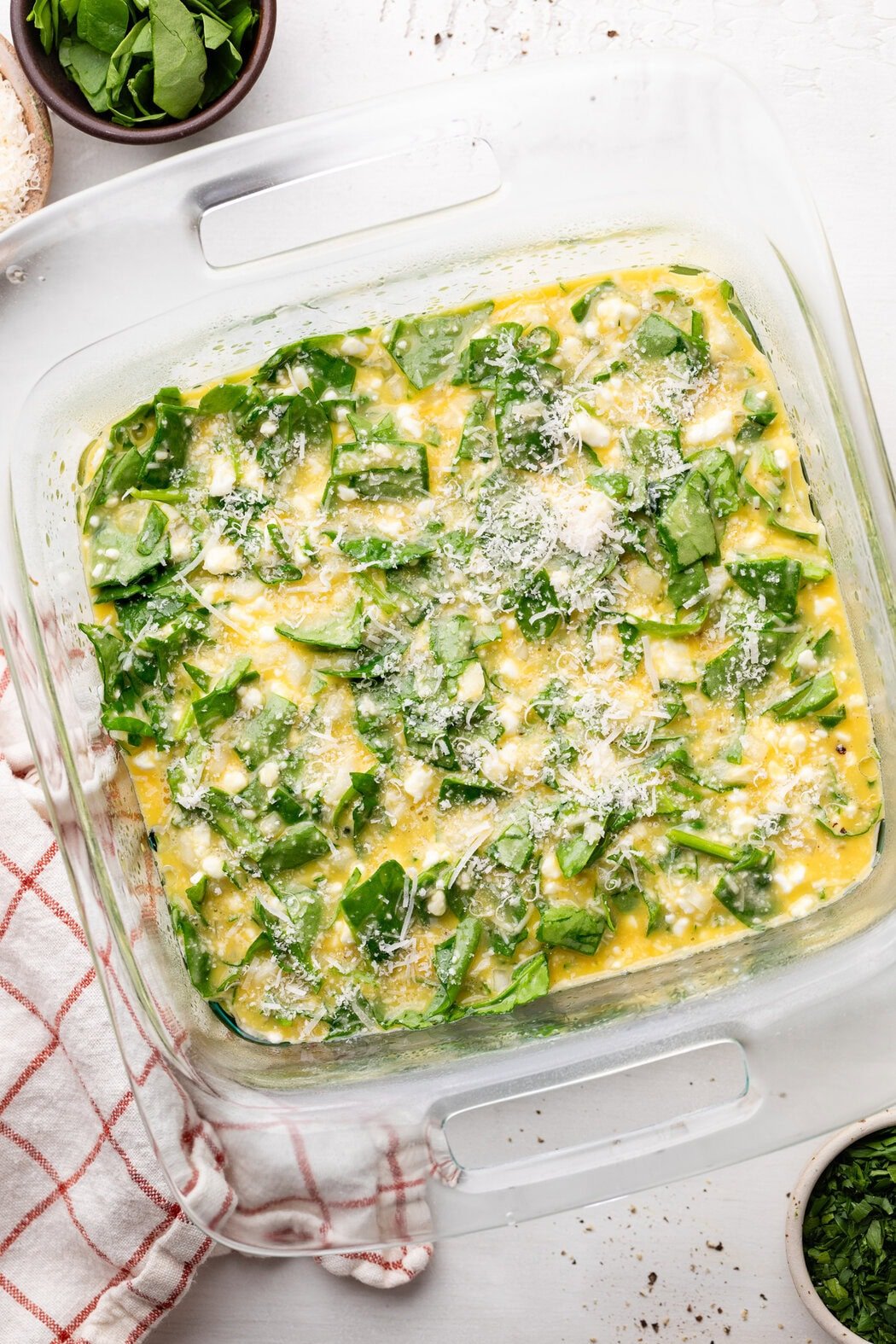 Overhead view of a glass baking dish filled with Cottage Cheese Egg Bake ingredients topped with parmesan cheese. 
