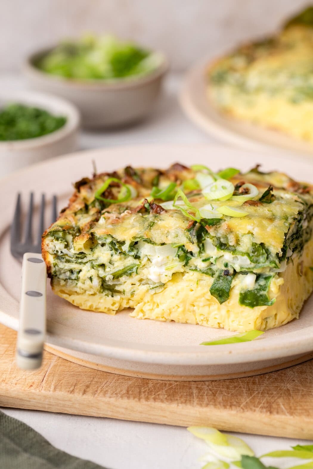 Close up view of a square piece of Cottage Cheese Egg Bake to show layers of green spinach and melty parmesan cheese with a fork on the side of the plate. 