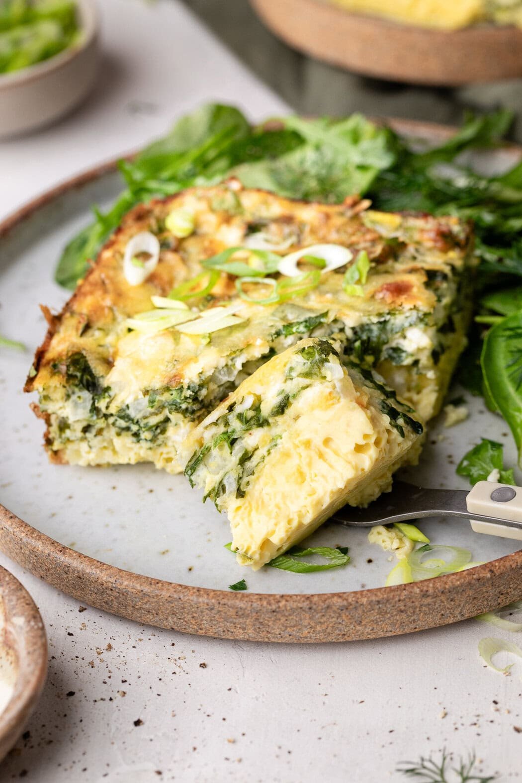 Close up view of a ceramic plate with a piece of Cottage Cheese Egg Bake on it next to greens. 