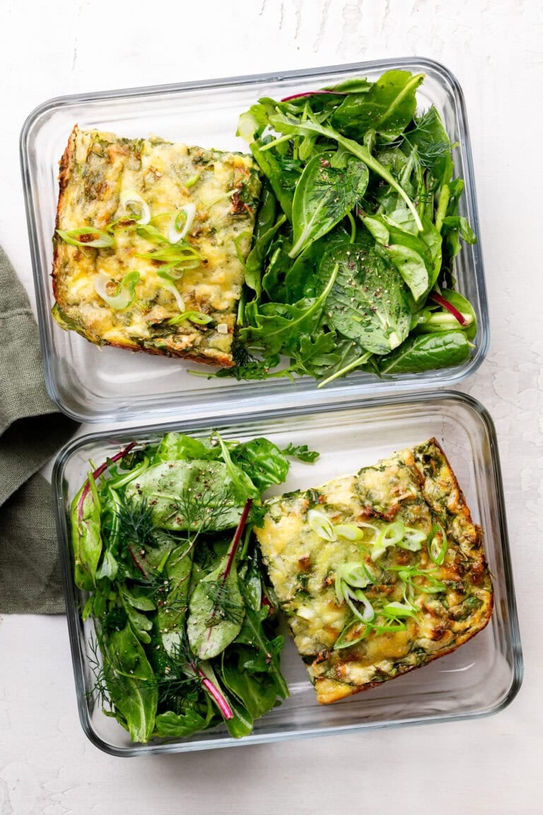 Overhead view of two glass meal prep containers filled with cottage cheese egg bake and fresh greens.