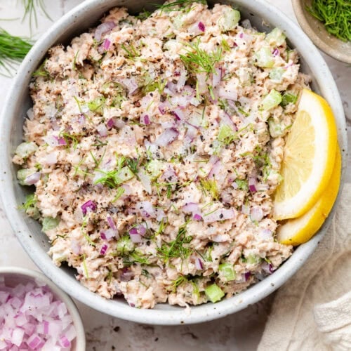 Overhead view of a bowl of My Easy 5-Minute Salmon Salad topped with fresh dill and garnished with lemon wedges.