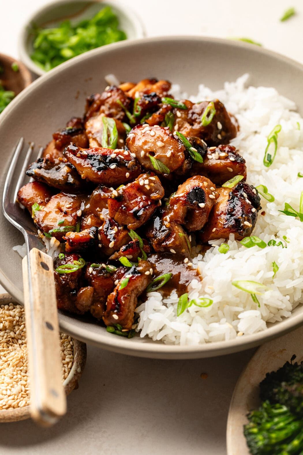 Close up view of a plate of Grilled Korean BBQ Chicken pieces and white rice on a white plate topped with green onions and sesame seeds. 