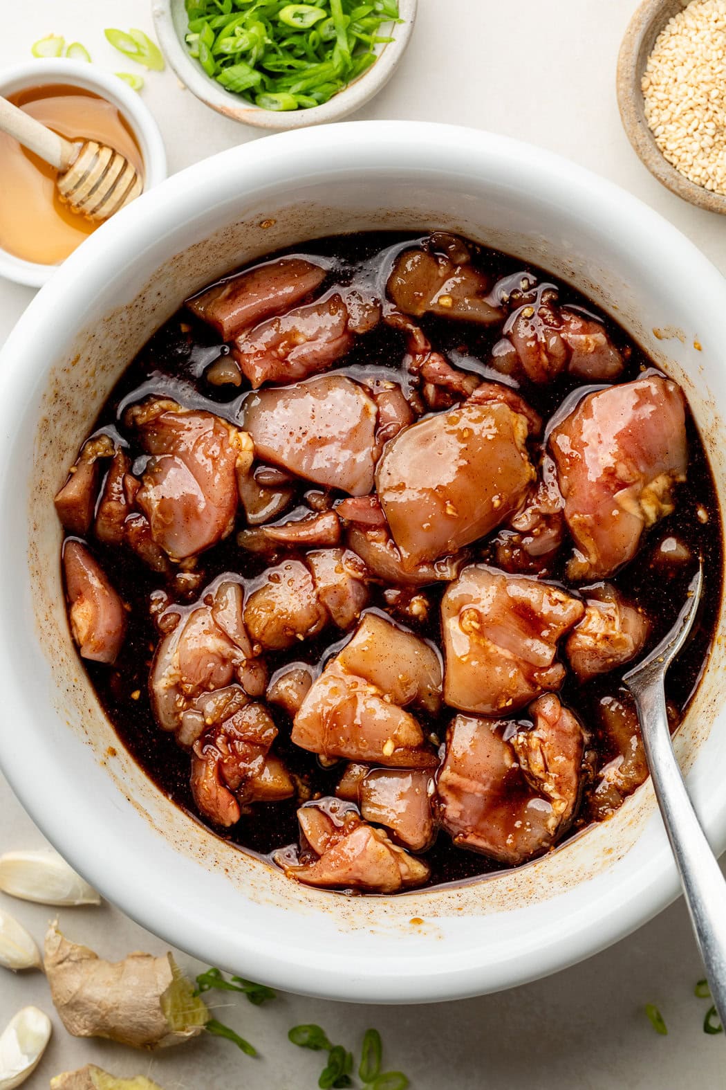Overhead view of a white bowl of chicken thighs marinating in a Korean BBQ sauce. 