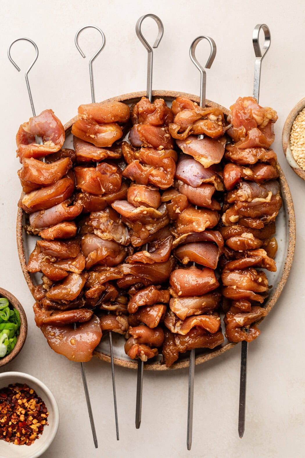 Close up view of a plate of metal skewers filled with marinated BBQ chicken ready for grilling. 