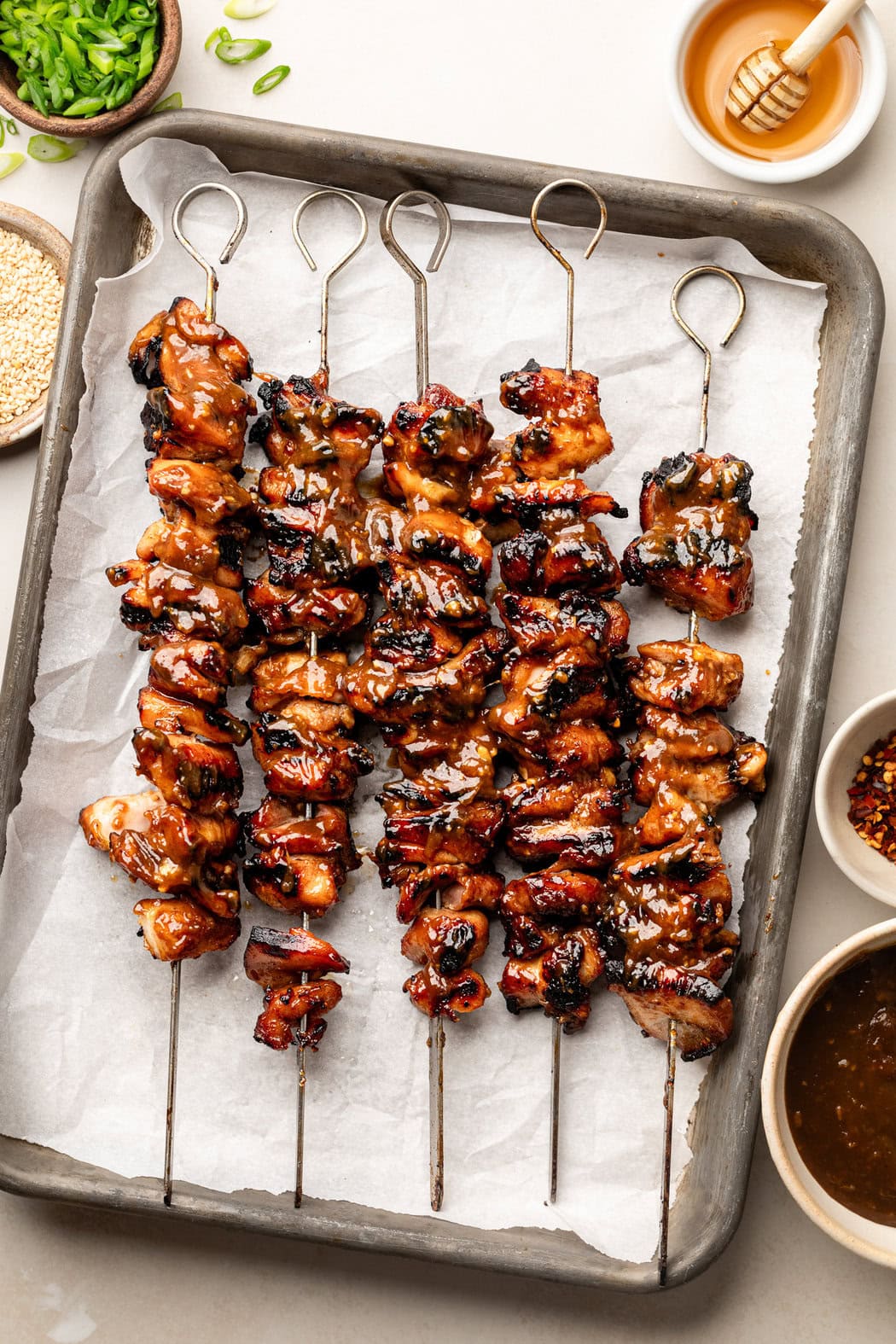 Overhead view of a sheet pan lined with parchment paper and filled with Grilled Korean BBQ Chicken skewers