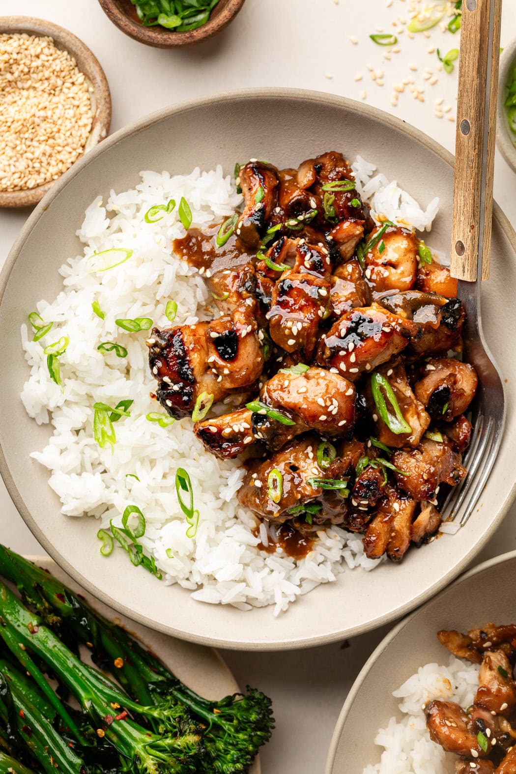 Overhead view of a plate of white rice and a side of Grilled Korean BBQ Chicken pieces topped with white sesame seeds and sliced green onions.