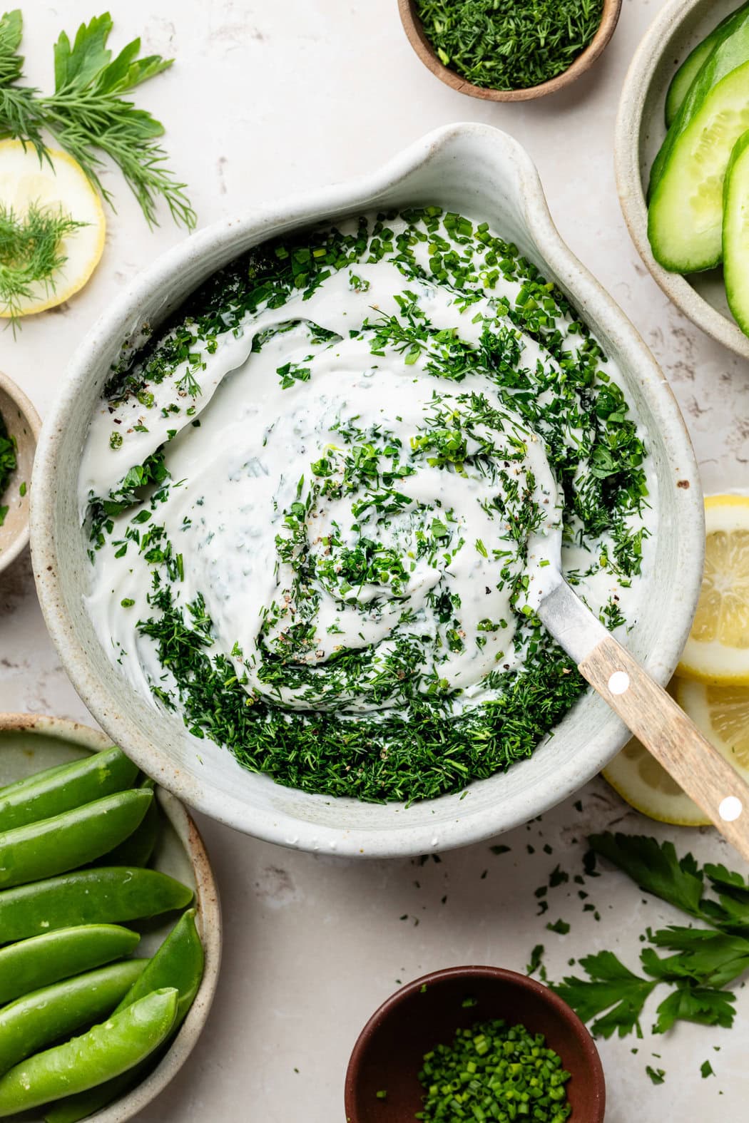 Overhead view of a bowl filled with whipped cottage cheese dip with fresh herbs on top ready for stirring. 