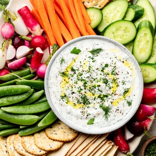 Overhead view of a bowl of whipped cottage cheese dip surrounded by raw vegetables and crackers.