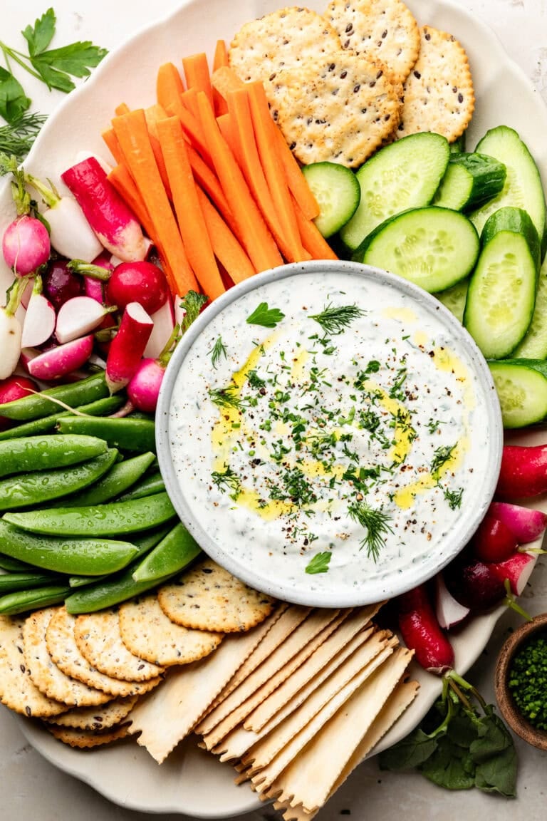 Overhead view of a colorful platter of fresh vegetables and crackers with a bowl of whipped cottage cheese dip in the center.