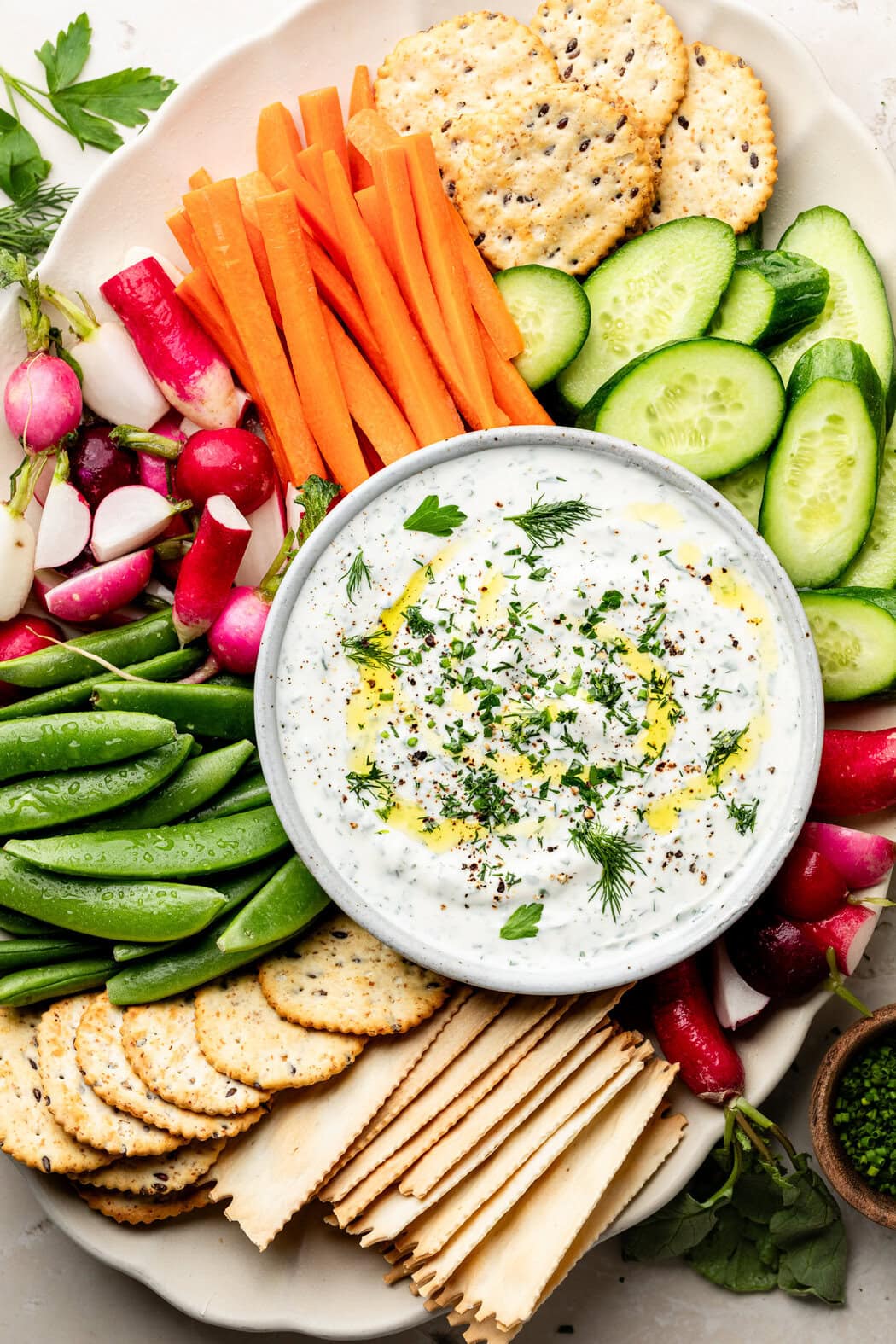 Overhead view of a bowl of whipped cottage cheese dip surrounded by fresh vegetables and crackers. 