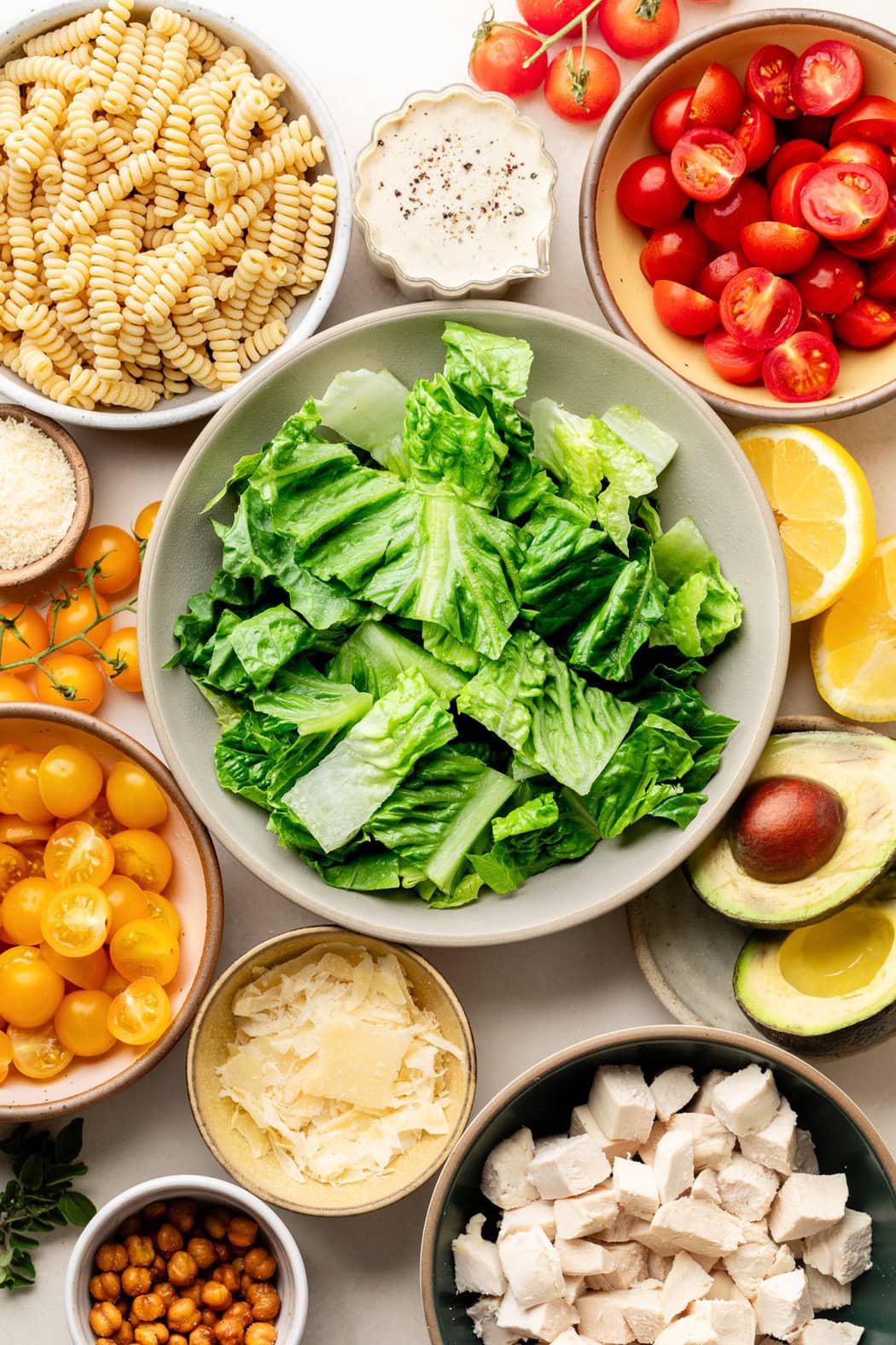 Overhead view of a variety of ingredients for Chicken Caesar Pasta Salad in different sized bowls. 