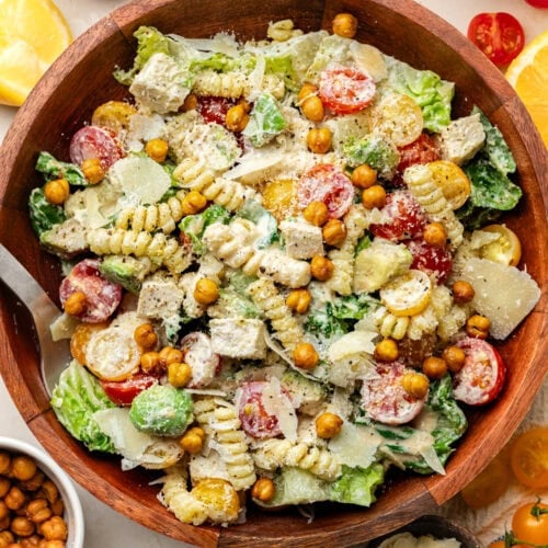 Overhead view of a large serving bowl filled with Chicken Caesar Pasta Salad topped with grated parmesan cheese and roasted chickpeas.