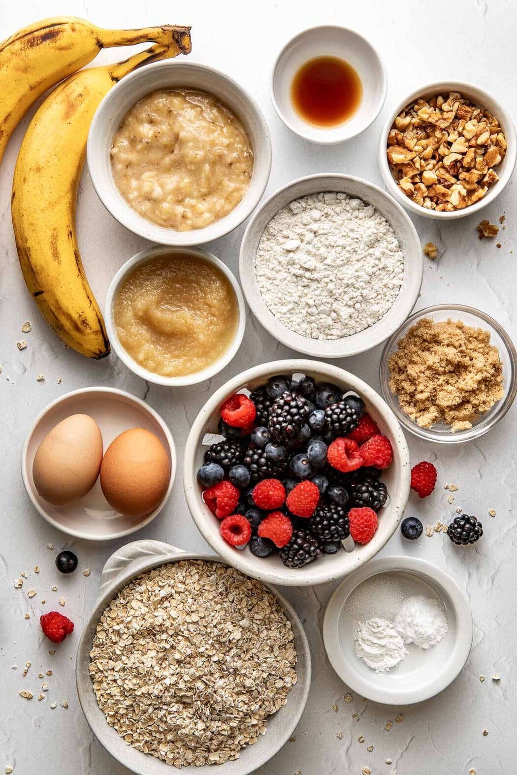 Overhead view of a variety of ingredients for Mixed Berry Baked Oatmeal Muffins in different sized bowls. 