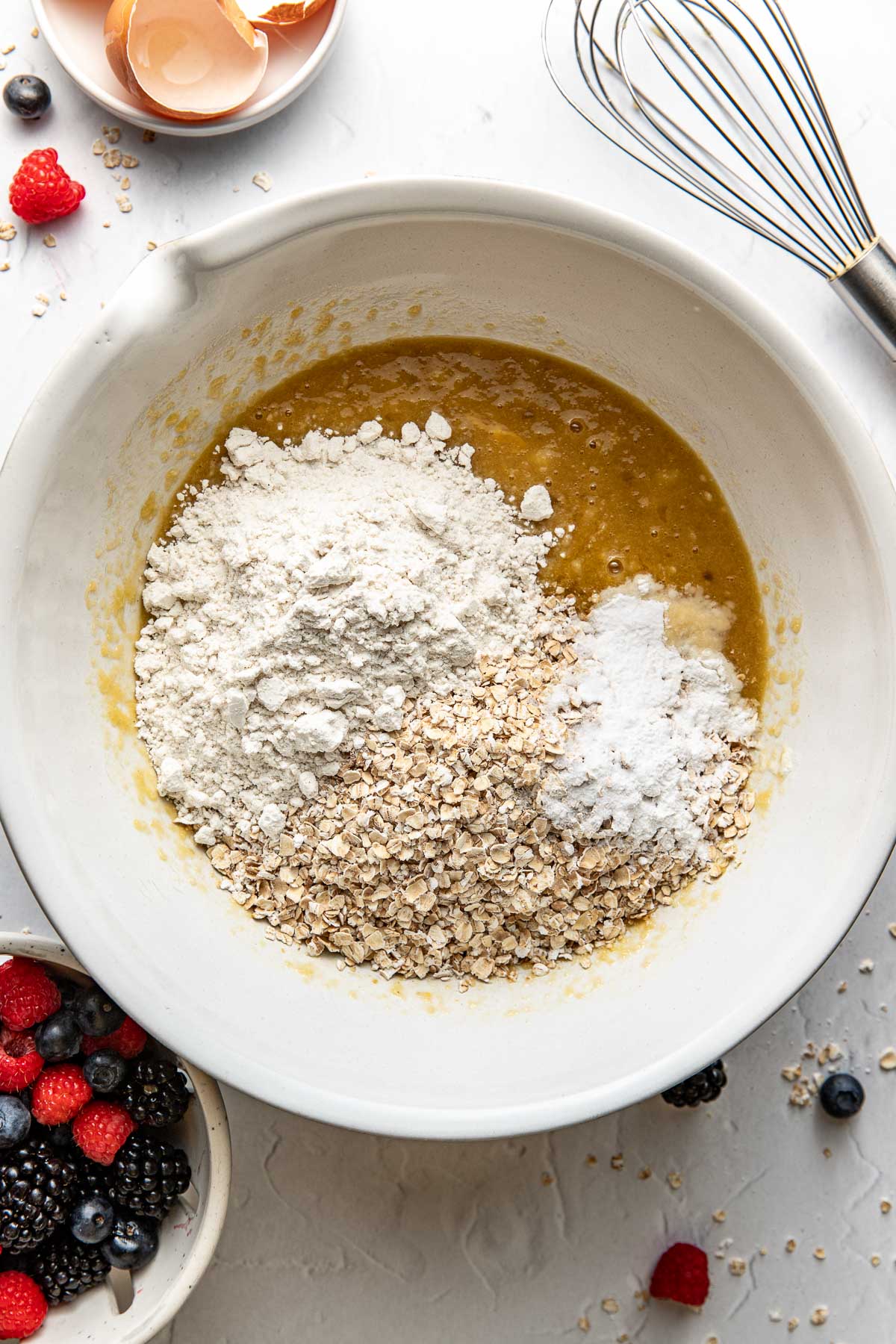 Overhead view of a white bowl filled with ingredients for Mixed Berry Baked Oatmeal Muffins ready for stirring. 