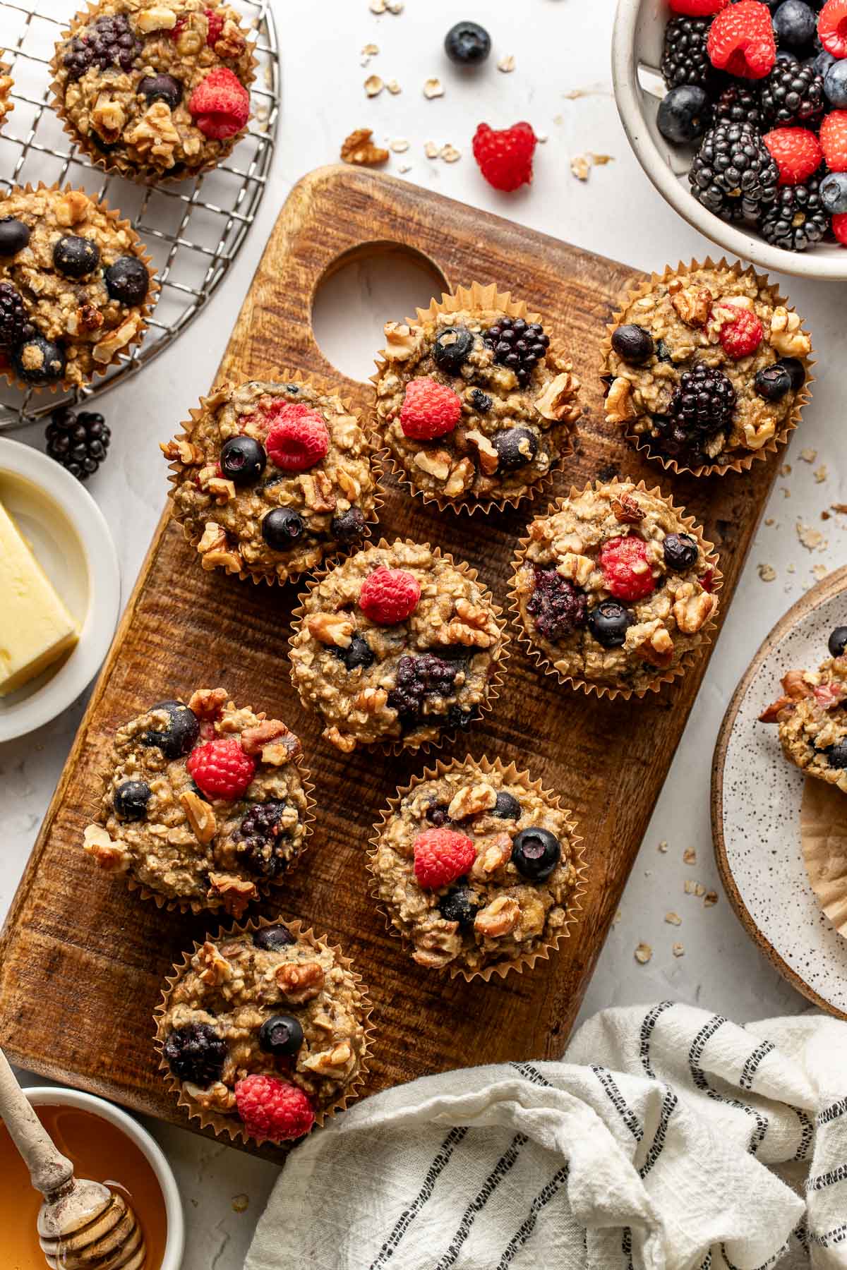 Overhead view of a wooden cutting board filled with freshly baked Mixed Berry Baked Oatmeal Muffins topped with walnut pieces. 
