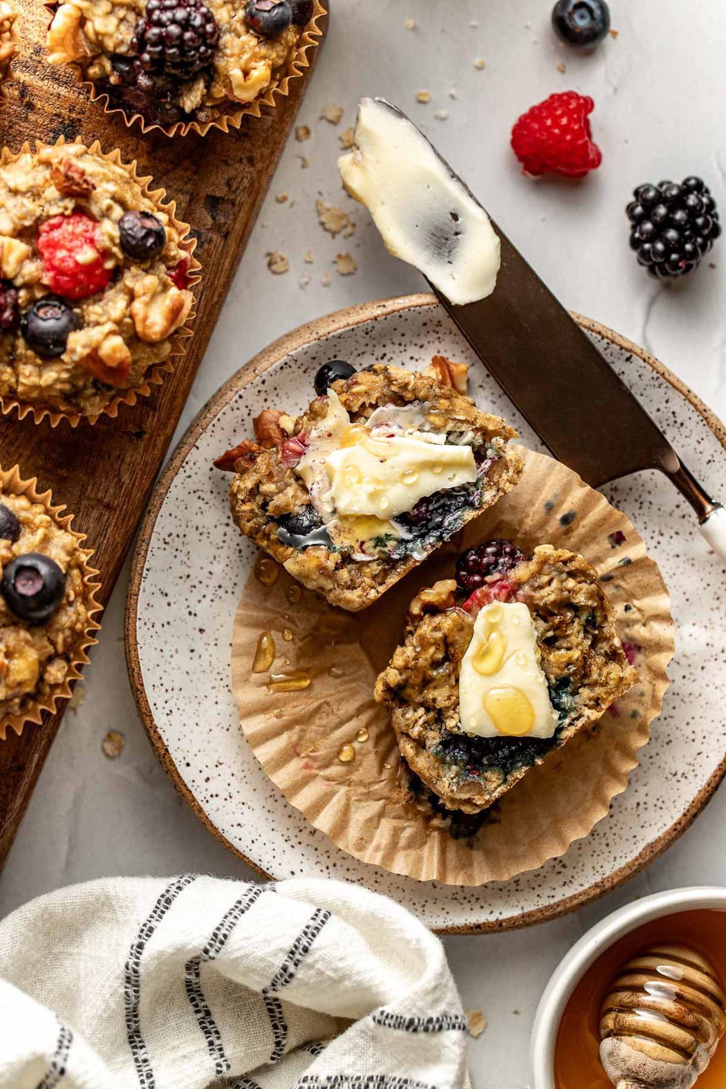 Overhead view of a Mixed Berry Baked Oatmeal Muffin cut in half and topped with butter and honey. 