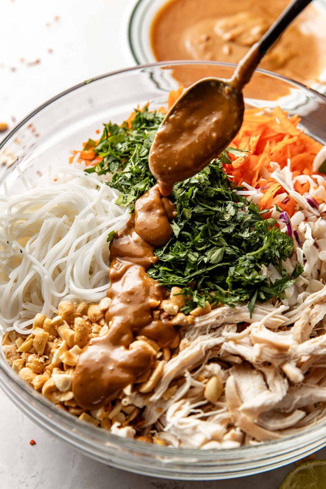 Overhead view of a bowl of Peanut Chicken ingredients with a spoon drizzling the sauce over the top. 