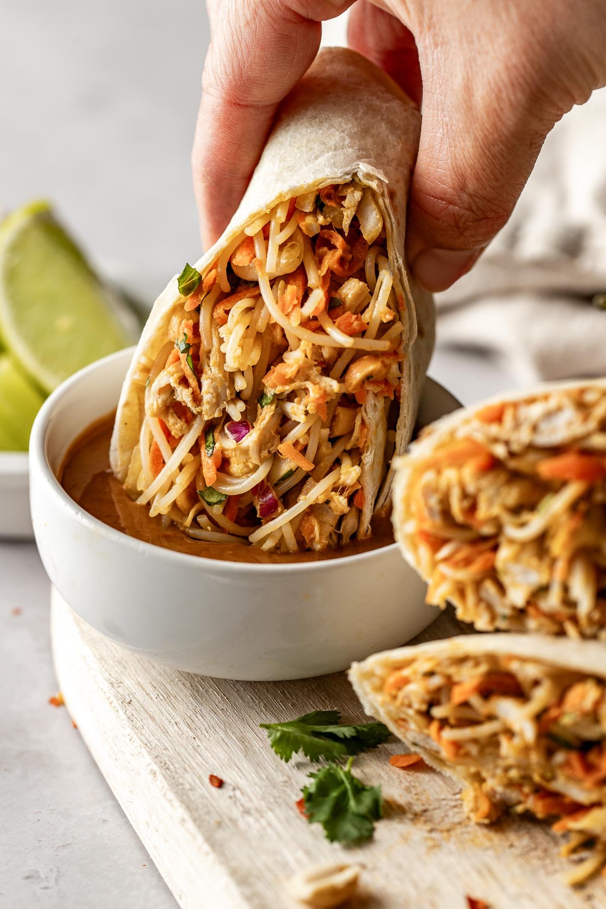 Close up view of a hand holding a Peanut Chicken Wrap and dipping into a bowl of peanut sauce. 