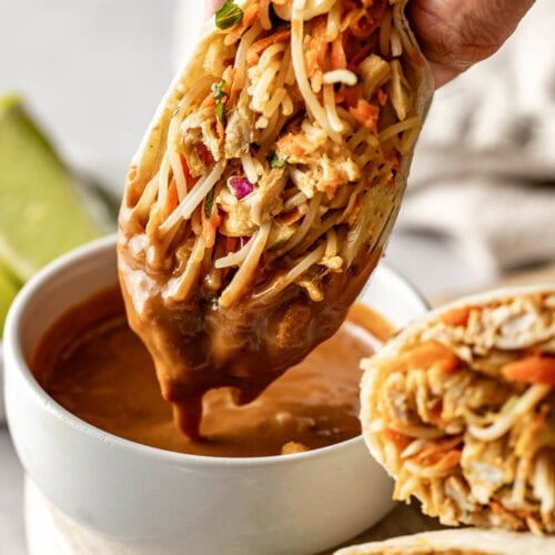 Close up view of a Peanut Chicken Wrap being dipped into a bowl of peanut sauce.