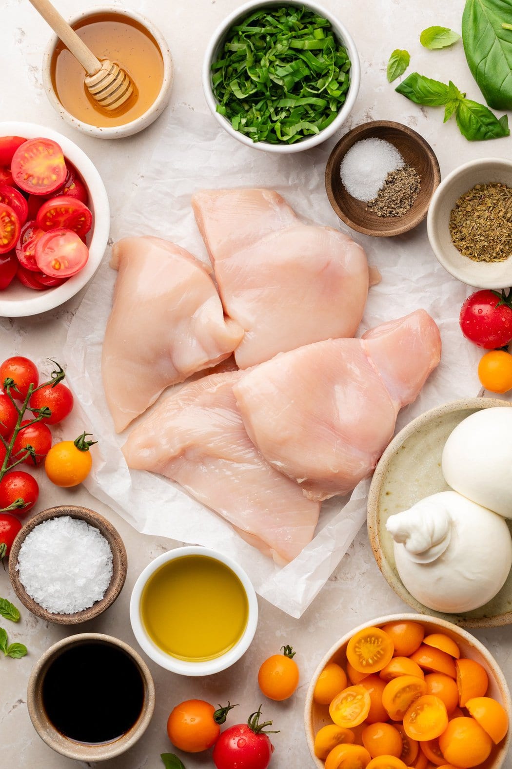 Overhead view of a variety of ingredients for Grilled Chicken Caprese with Burrata in different sized bowls. 