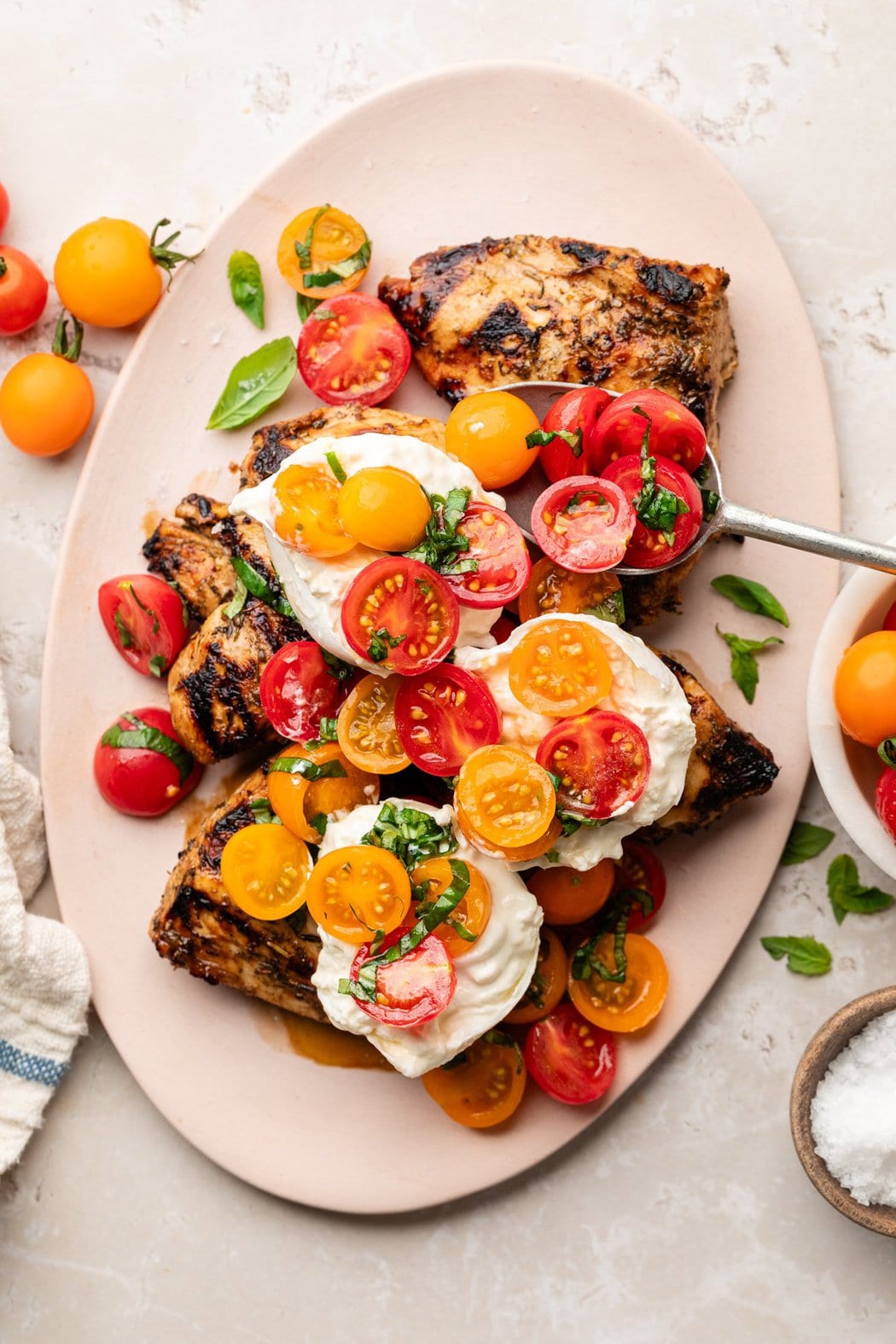 Overhead view of a platter of Grilled Chicken Caprese with Burrata topped with fresh cherry tomatoes and basil. 