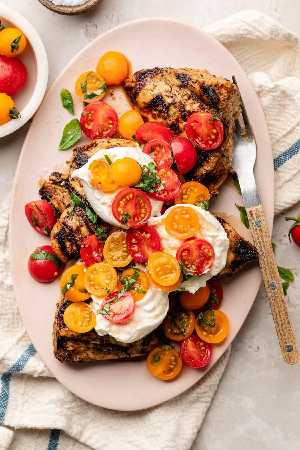 Overhead view of a platter filled with Grilled Chicken Caprese with Burrata topped with fresh basil.
