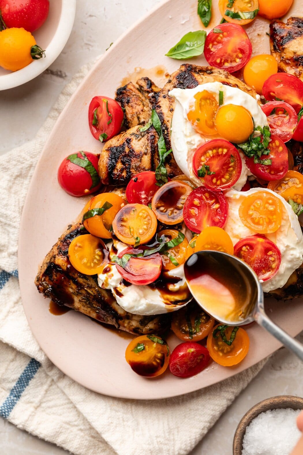 Close up view of a spoon drizzling balsamic reduction over Grilled Chicken Caprese with Burrata. 