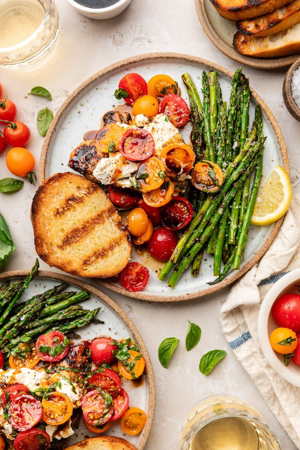 Overhead view of a plate of Grilled Chicken Caprese with Burrata and a piece of toasted garlic bread and a side of asparagus. 