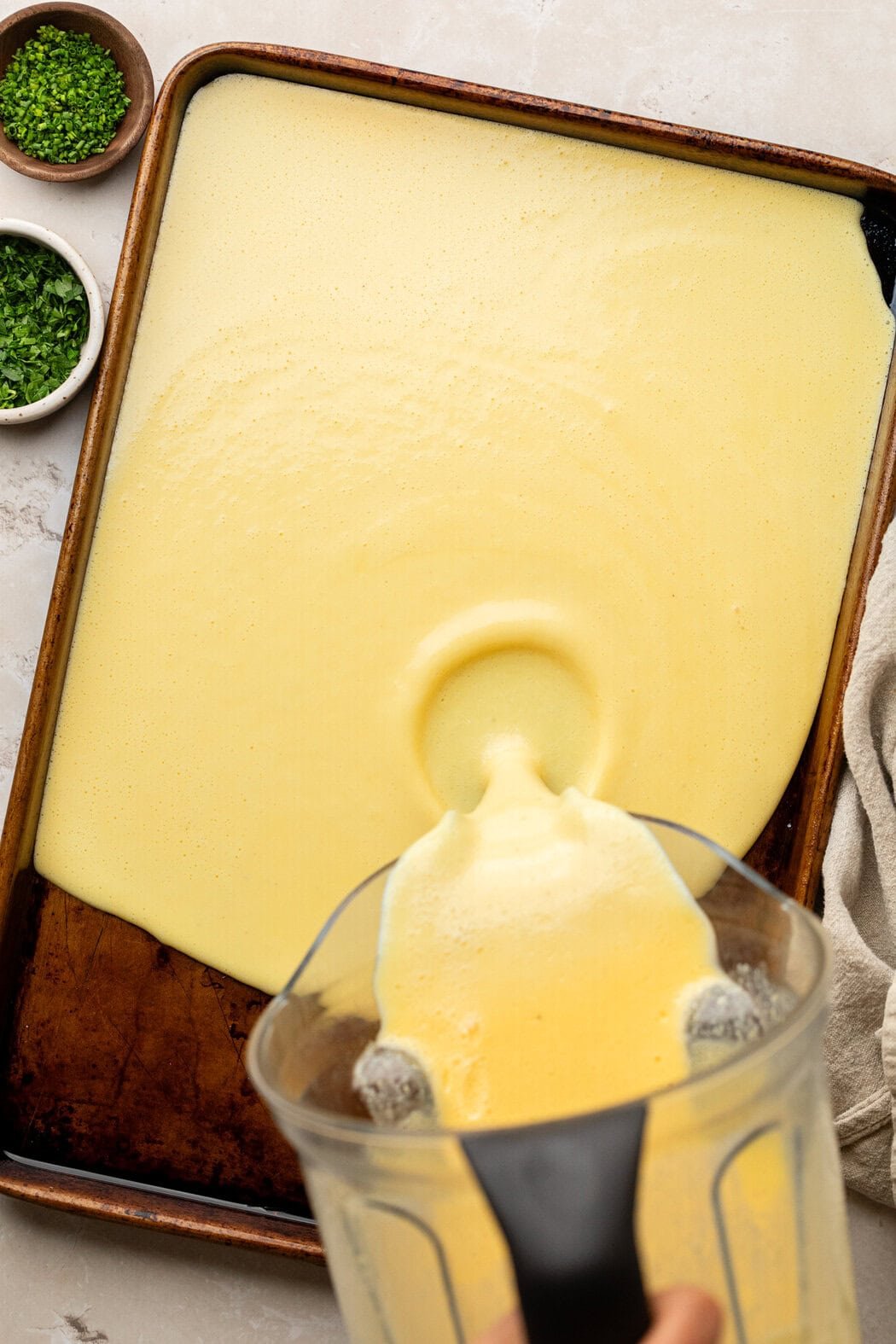 Overhead view of a metal sheet pan with a hand pouring an egg mixture from a blender. 