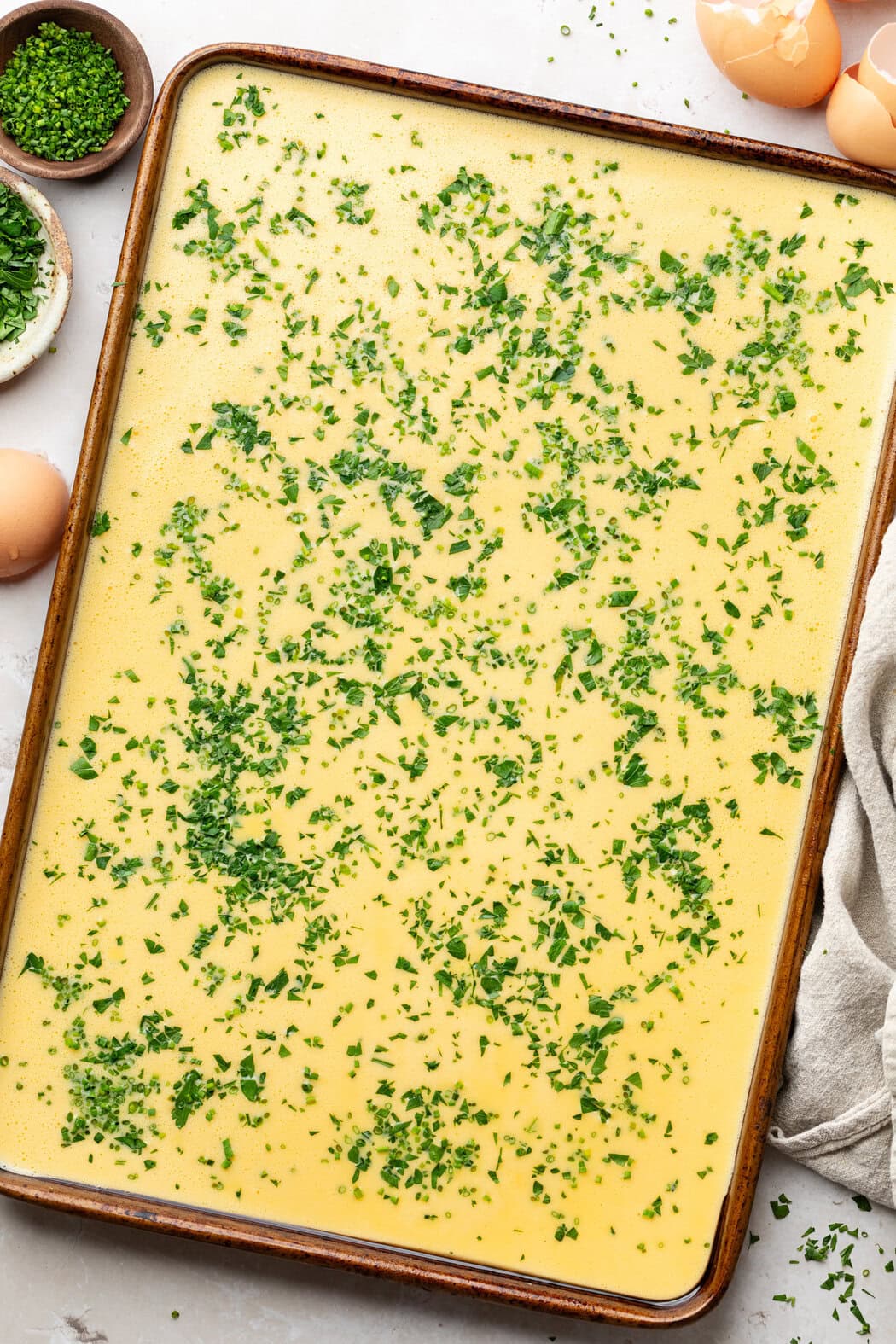 Overhead view of a metal sheet pan filled with sheet pan egg mixture and topped with fresh herbs. 