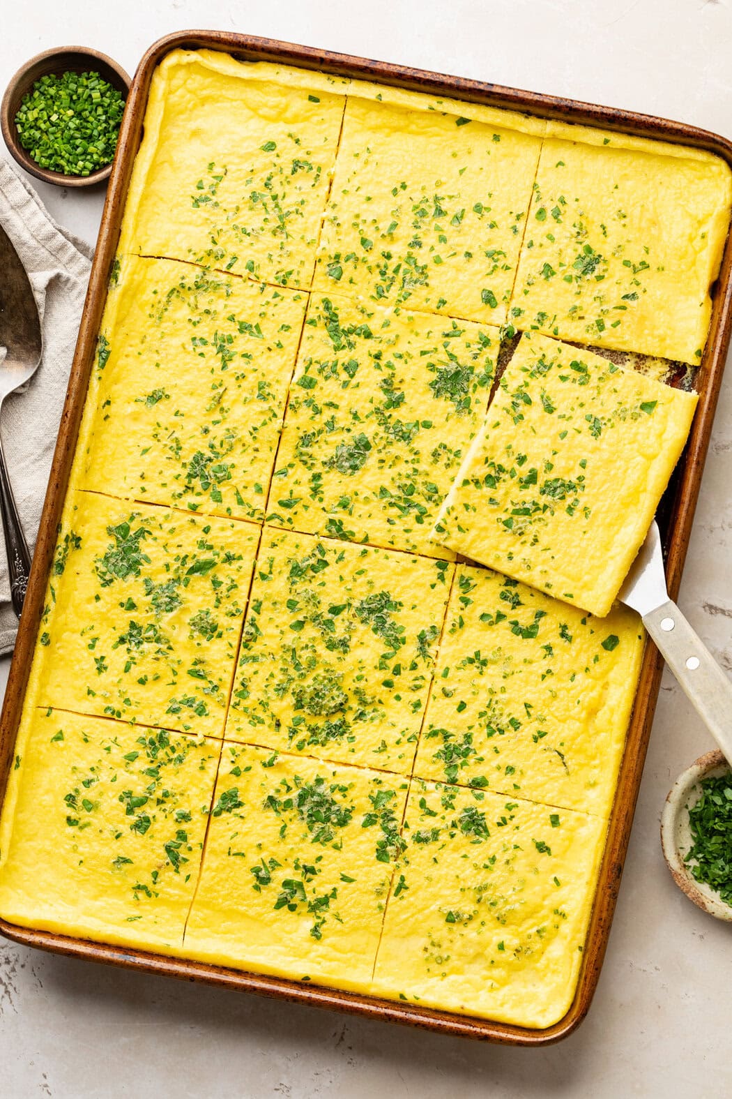 Close up view of a metal sheet pan with cottage cheese egg pieces cut into squares and topped with fresh herbs. 