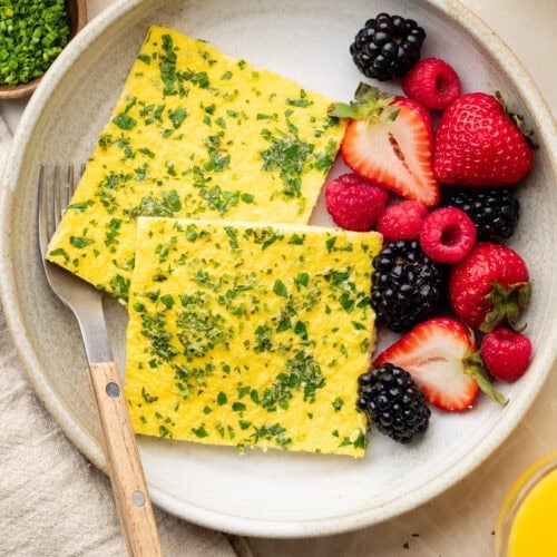 Overhead view of two squares of sheet pan eggs on a plate with colorful berries on the side.