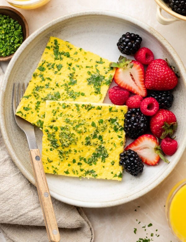 Overhead view of two squares of sheet pan eggs on a plate with colorful berries on the side.