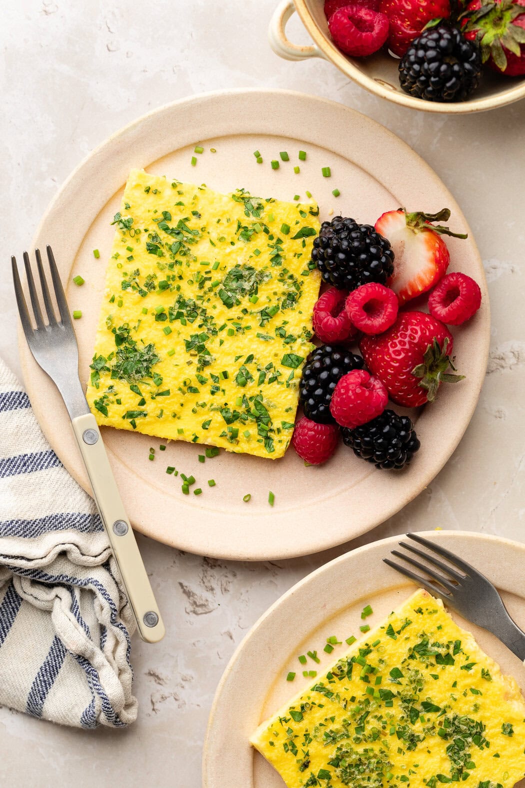 Overhead view of two plates of Sheet Pan Eggs with Cottage Cheese pieces and berries on the side. 