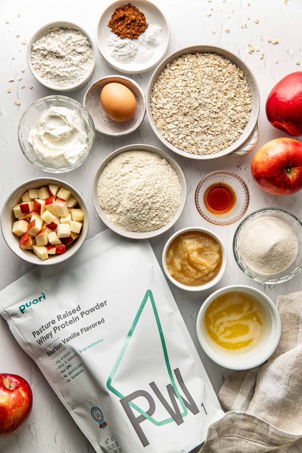 Overhead view of a variety of ingredients for Apple Cinnamon Protein Muffins in different sized bowls. 