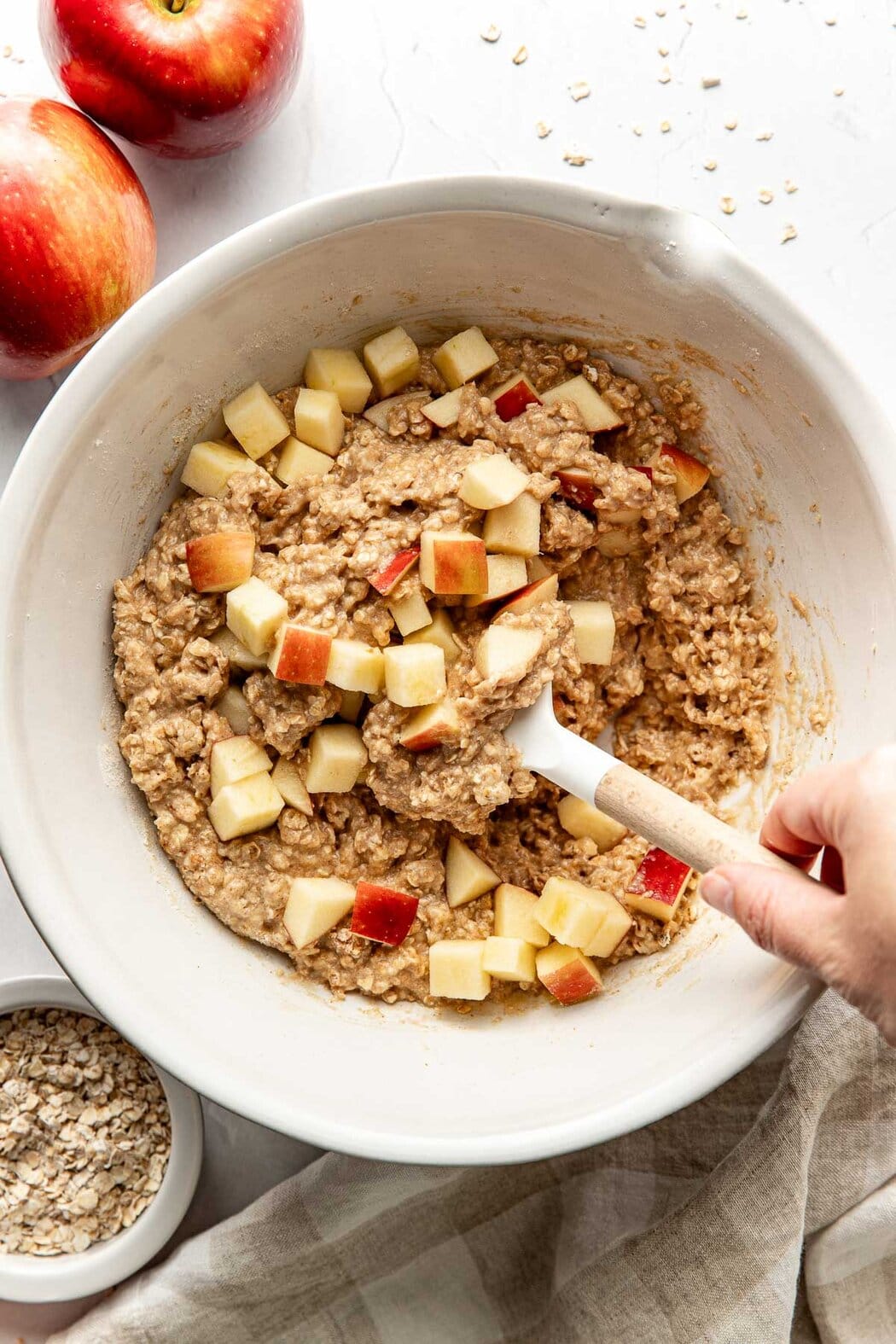 Overhead view of a hand stirring Apple Cinnamon Protein Muffin batter with a spatula. 