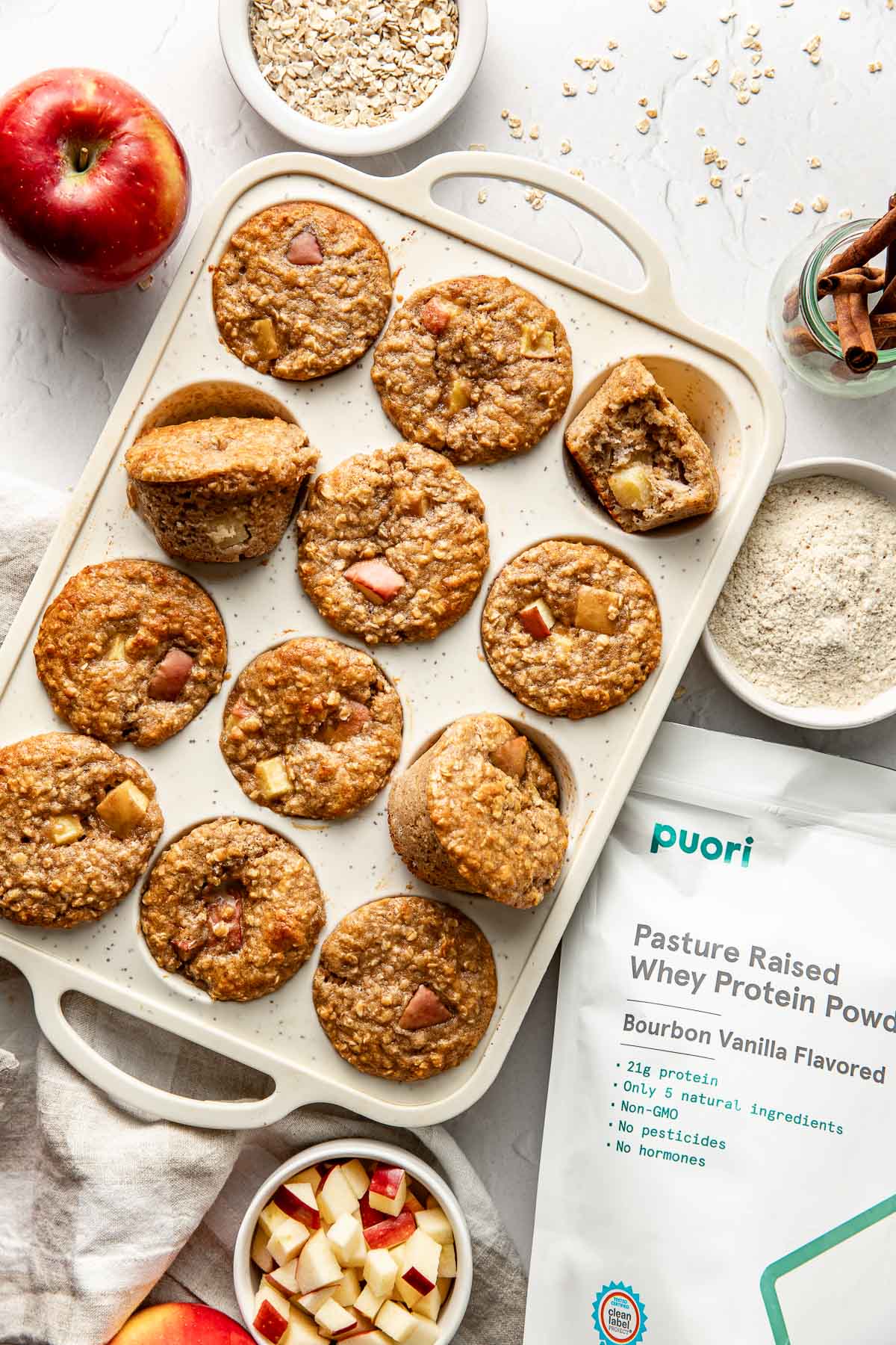 Close up view of a freshly baked pan of Apple Cinnamon Protein Muffins with a bag of puori protein on the side. 