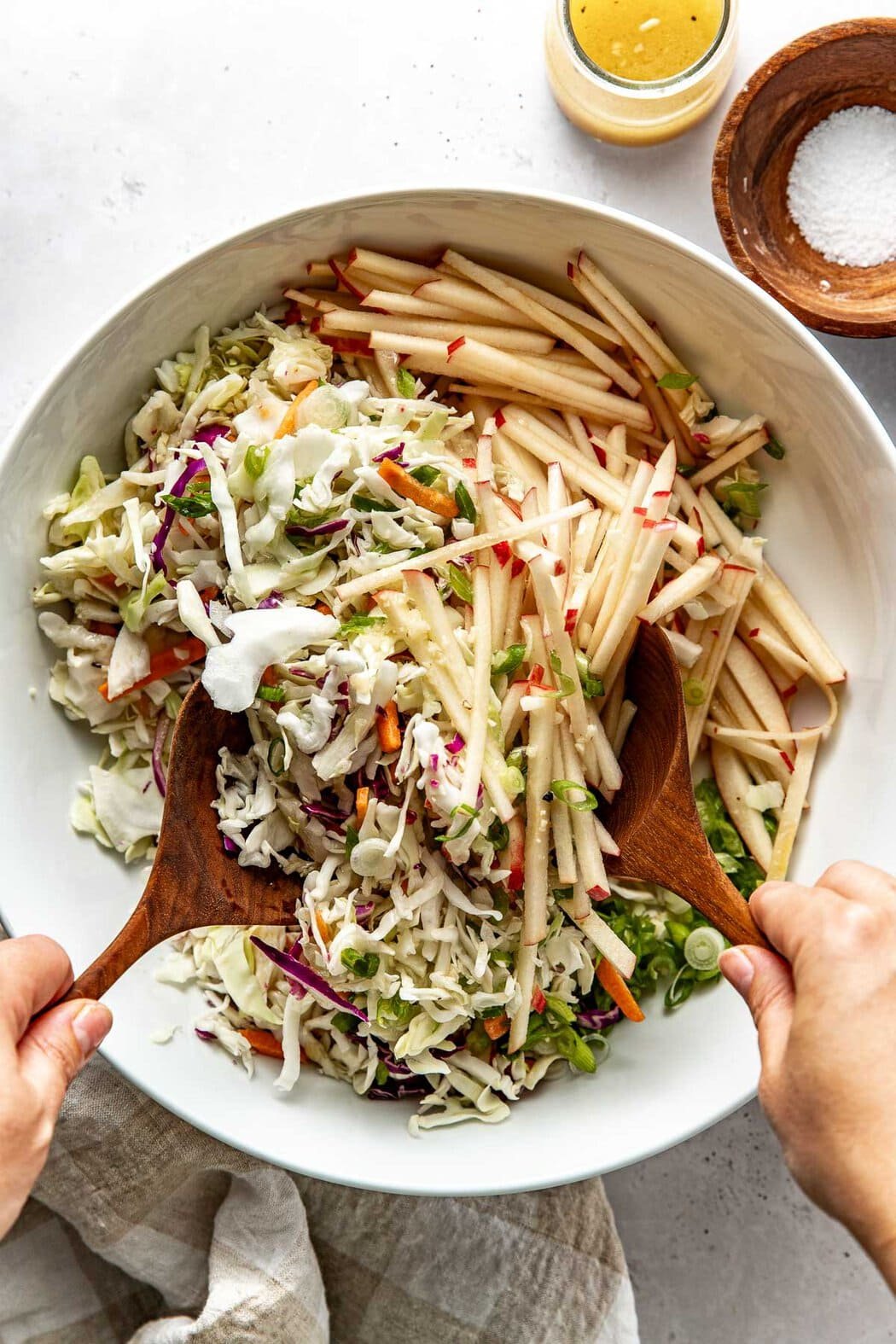 Overhead view of a bowl of apple slaw being tossed with two wooden spoons. 