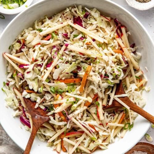 Overhead view of a white bowl filled with colorful Apple Slaw topped with black pepper and green onions.