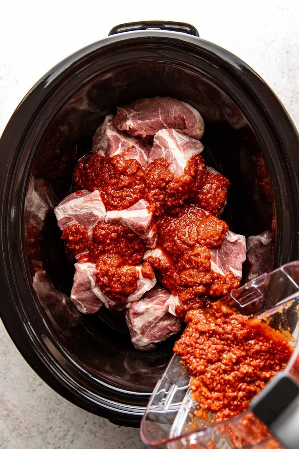 Overhead view of a crockpot filled with chunks of pork and Al Pastor sauce mixture being poured over the top. 