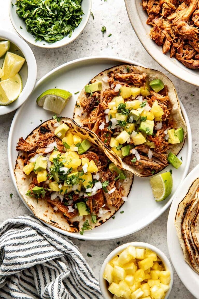 Overhead view of a plate with two tacos al pastor topped with fresh pineapple.