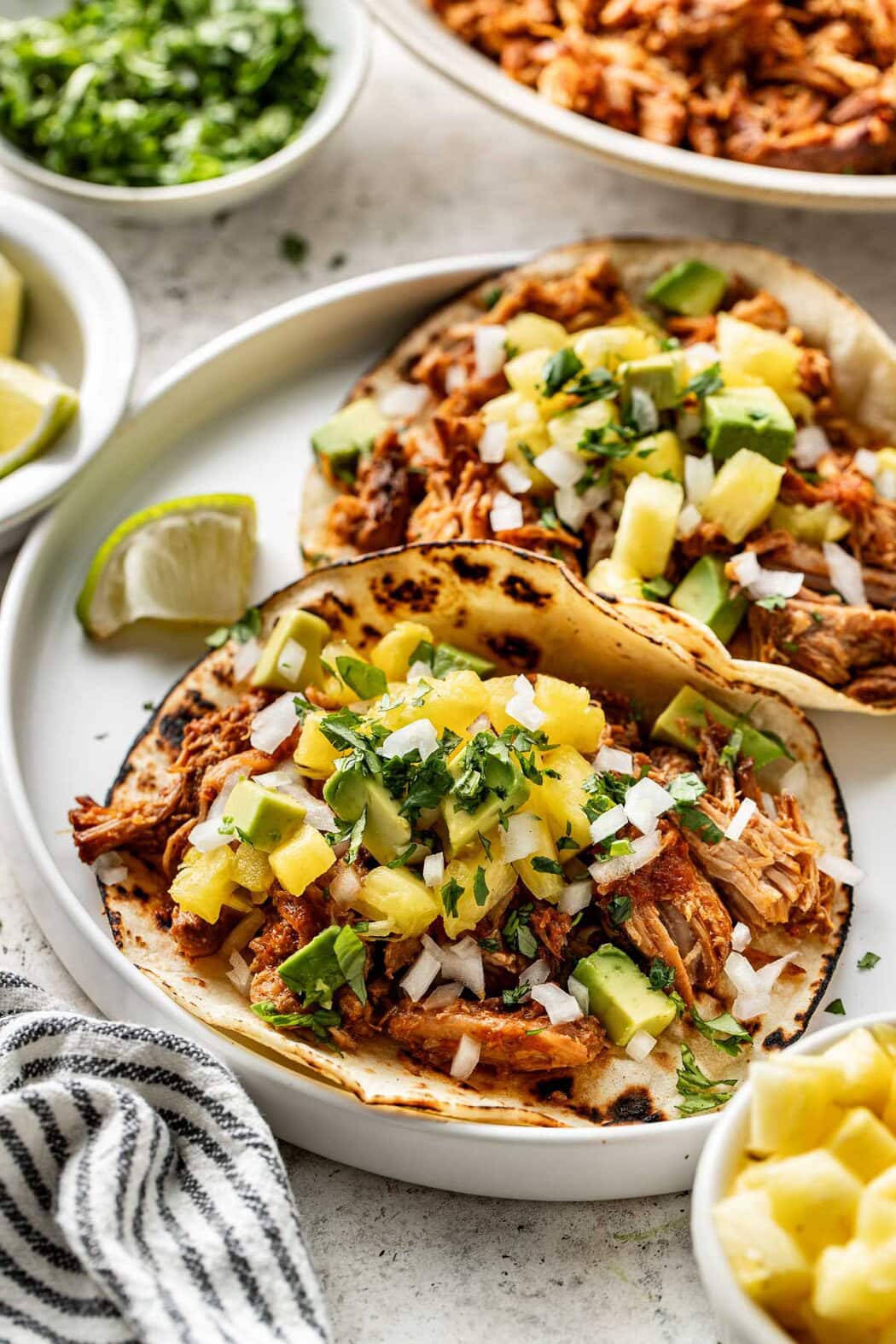 Close up view of Crockpot Tacos Al Pastor in tortillas on a plate, topped with fresh pineapple and cilantro. 