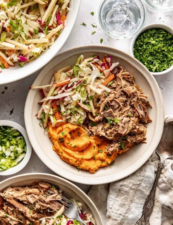 Overhead view white bowl with servings of mashed sweet potato, apple cider pork, and apple slaw