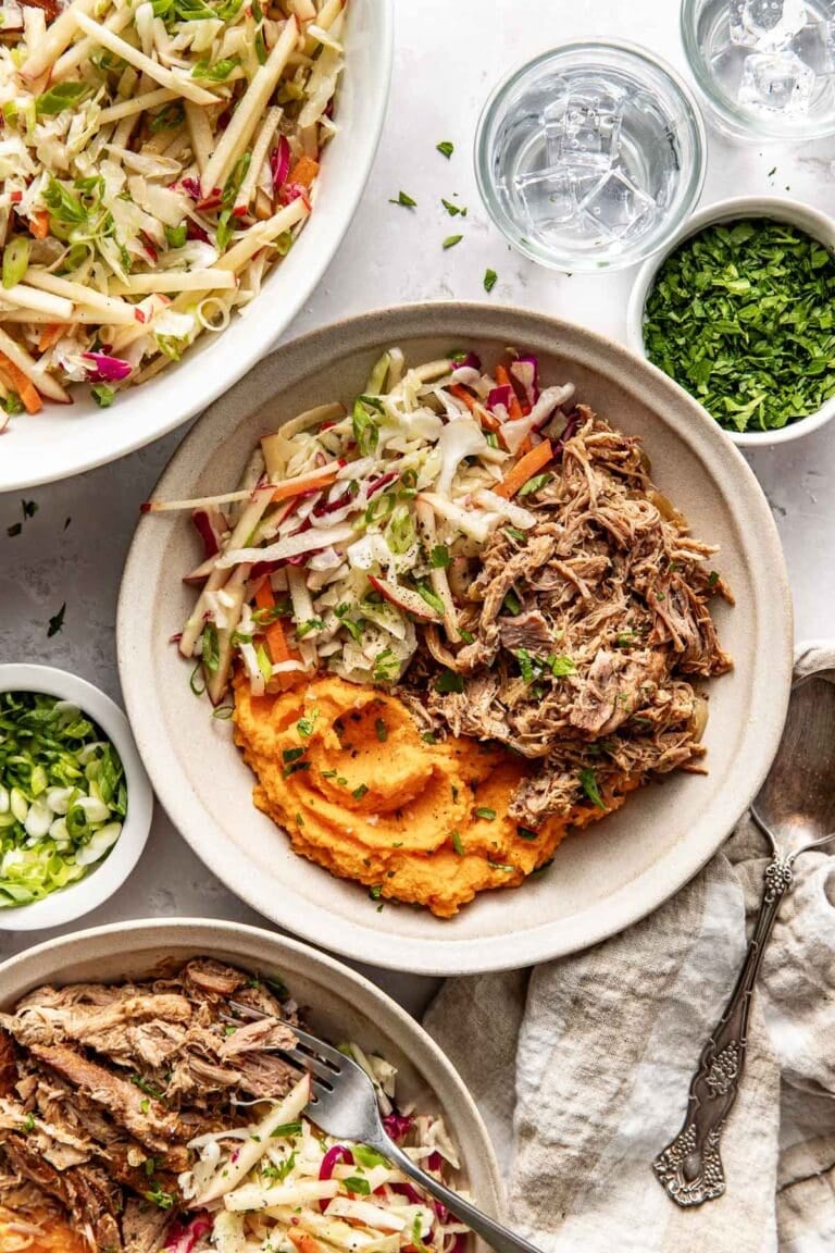 A white bowl with servings of mashed sweet potato, apple cider pork, and apple slaw.