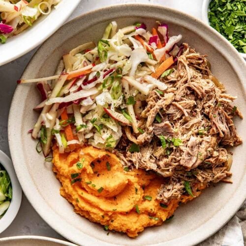 Close up view of a Crockpot Apple Cider Pork Bowl topped with black pepper and fresh herbs.