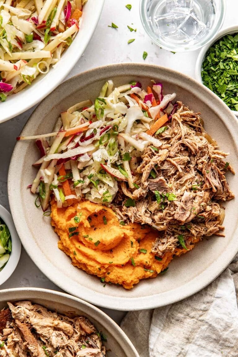 Close up view of a Crockpot Apple Cider Pork Bowl topped with black pepper and fresh herbs.