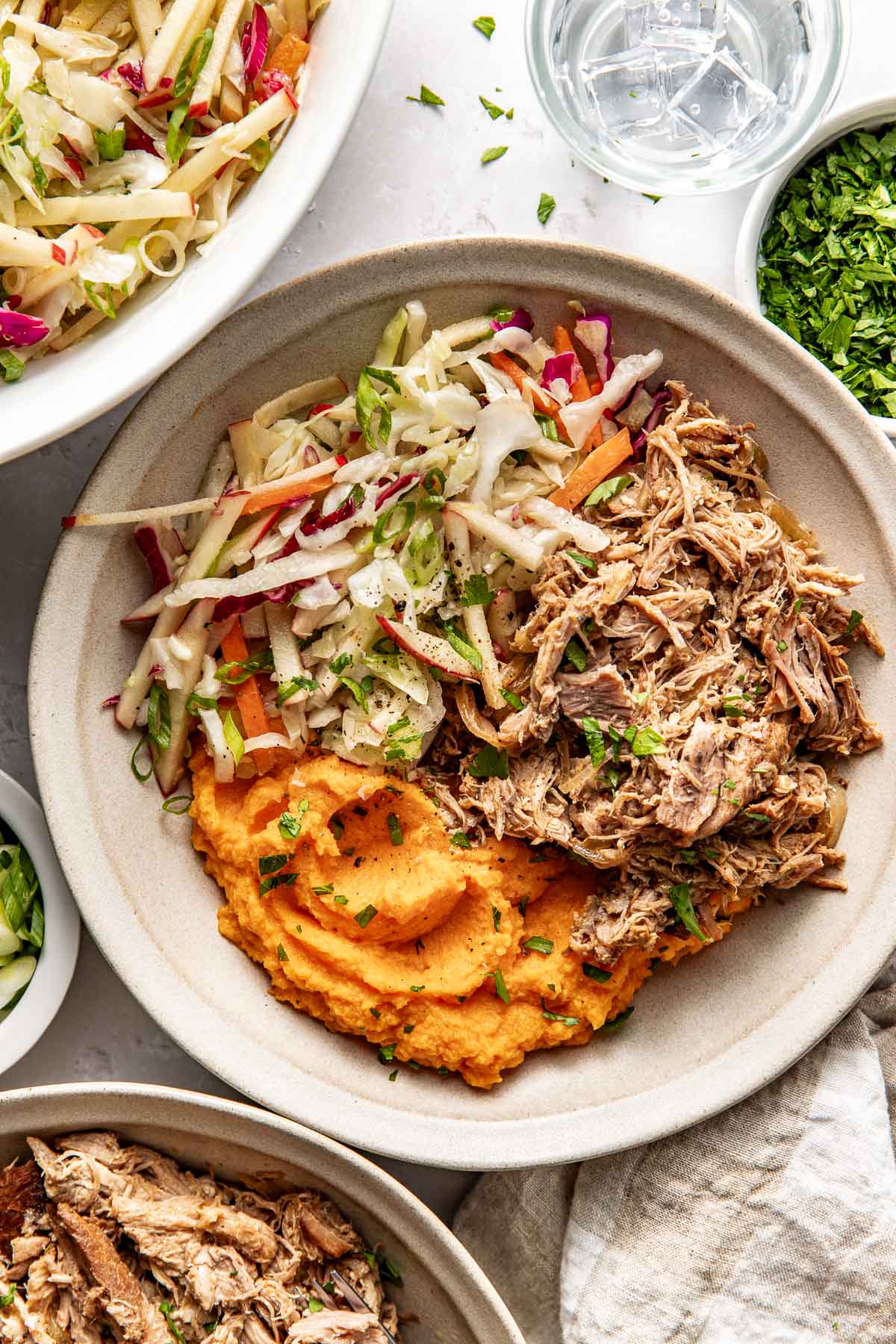 Overhead view of a white bowl filled with deep orange mashed sweet potatoes, pulled pork, and colorful fresh apple slaw. 